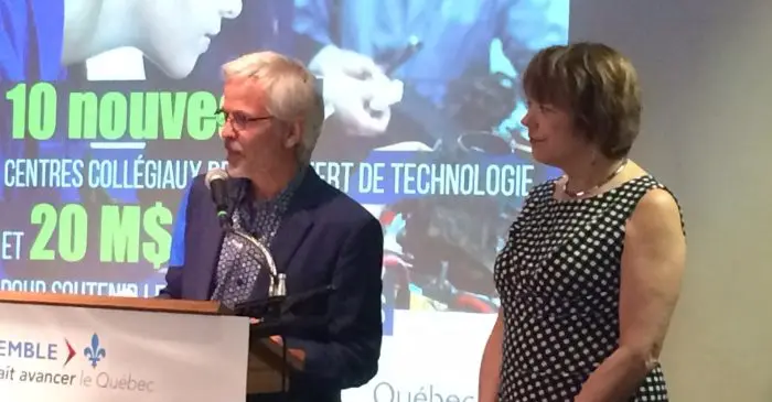 Deux personnes se tiennent sur un podium lors d'une présentation. L'homme parle dans un micro tandis que la femme se tient à ses côtés. Derrière eux, une banderole colorée met en évidence le centre de recherche de l'ECN, un Centre collégial de transfert technologique (CCTT).