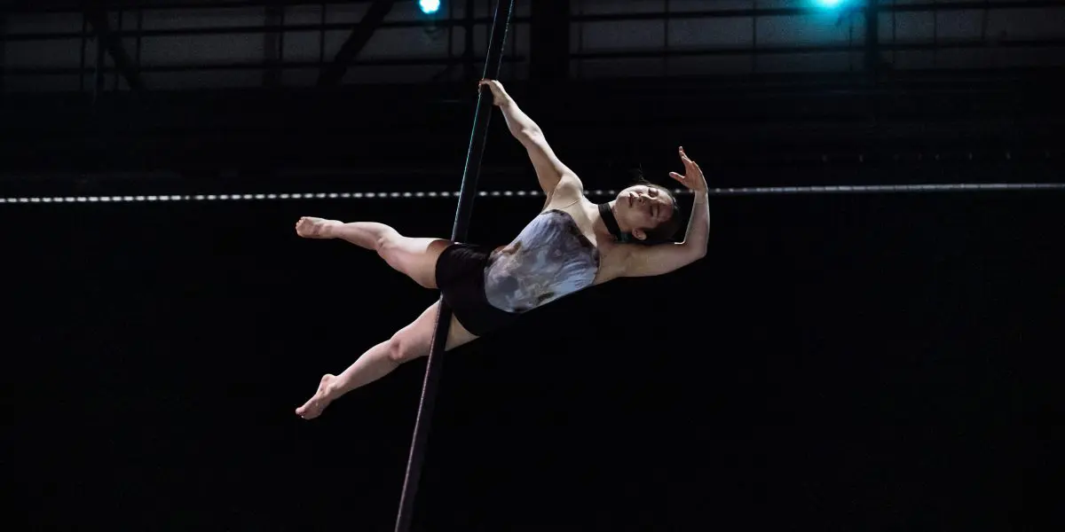 L'artiste aérienne Minji Kim prend une pose élégante alors qu'elle est suspendue horizontalement à une corde verticale, les lumières de la scène l'éclairant sur un fond sombre.
