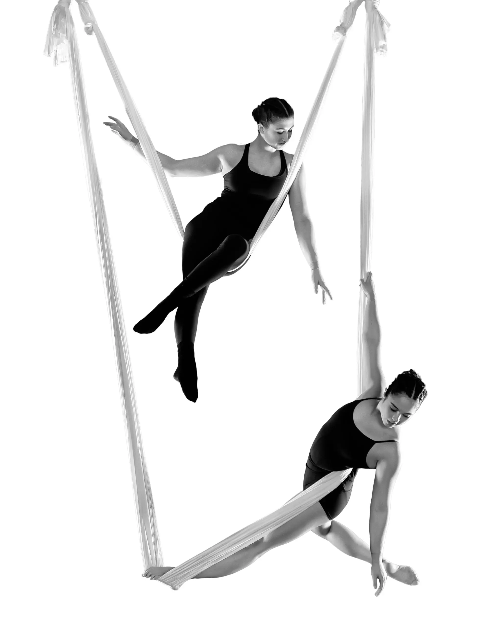 Sydney Ramirez et Brianna MacDonald exécutent une routine aérienne en soie, suspendues dans les airs sur un fond blanc. Elles portent des tenues noires et prennent des poses élégantes en s'agrippant et en se balançant sur le tissu.