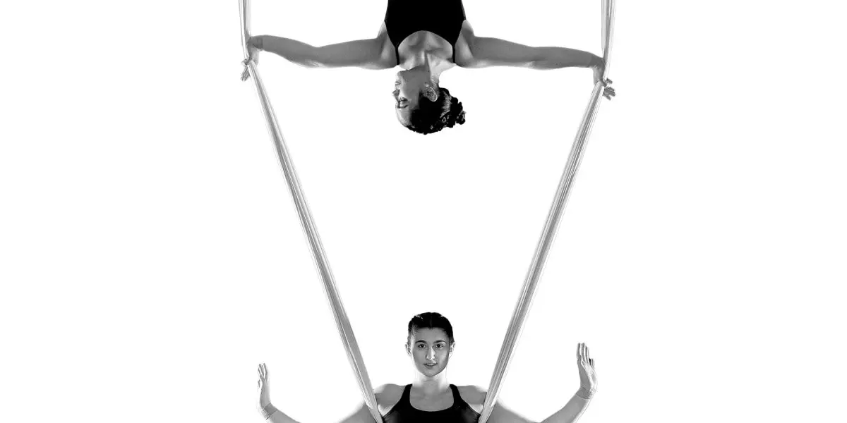 Sydney Ramirez et Brianna MacDonald exécutent un numéro d'acrobatie aérienne sur soie ; l'une est suspendue à l'envers au sommet en tenant les soies, tandis que l'autre est debout en dessous d'elle, toutes deux vêtues de justaucorps et posant gracieusement sur un fond blanc.
