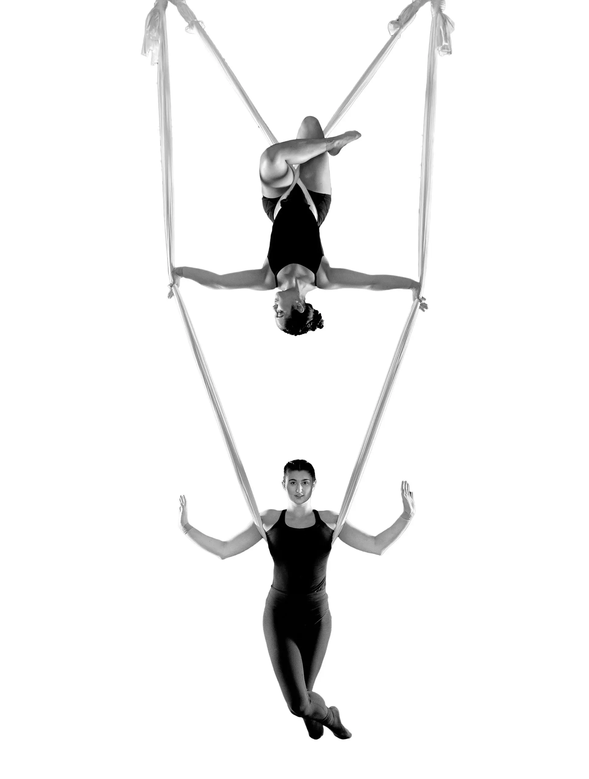 Sydney Ramirez et Brianna MacDonald exécutent un numéro d'acrobatie aérienne sur soie ; l'une est suspendue à l'envers au sommet en tenant les soies, tandis que l'autre est debout en dessous d'elle, toutes deux vêtues de justaucorps et posant gracieusement sur un fond blanc.
