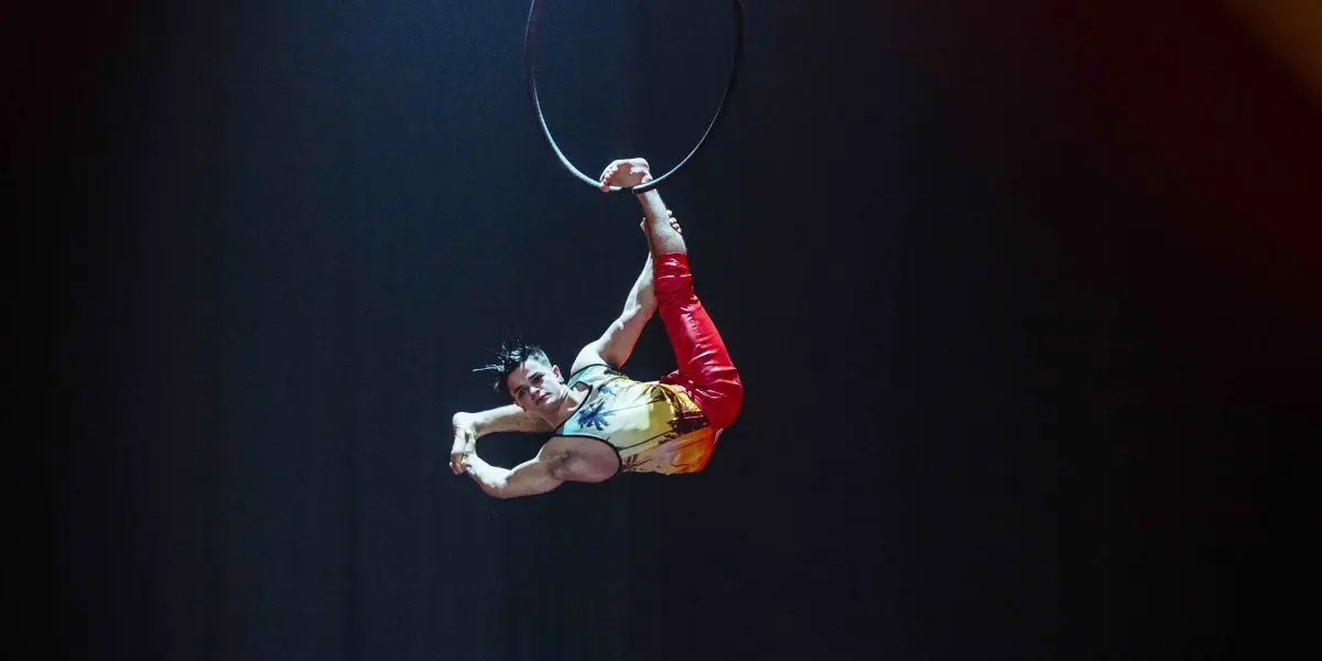 L'artiste de cirque Enzo Prebre exécute un numéro de cerceau aérien, suspendu la tête en bas avec une jambe accrochée au cerceau et l'autre tendue vers le haut, faisant preuve d'une force et d'une souplesse impressionnantes sous les projecteurs.