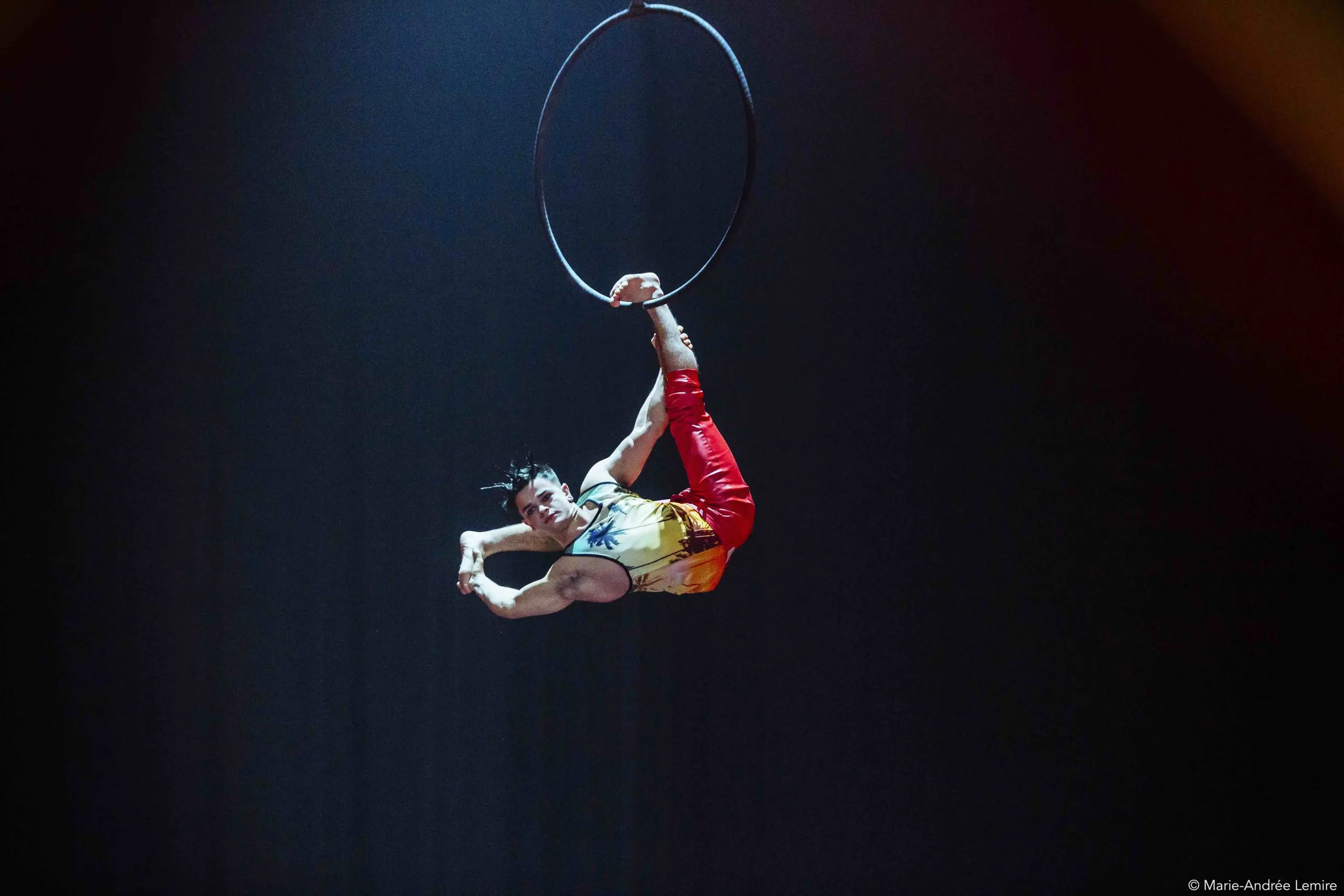 L'artiste de cirque Enzo Prebre exécute un numéro de cerceau aérien, suspendu la tête en bas avec une jambe accrochée au cerceau et l'autre tendue vers le haut, faisant preuve d'une force et d'une souplesse impressionnantes sous les projecteurs.
