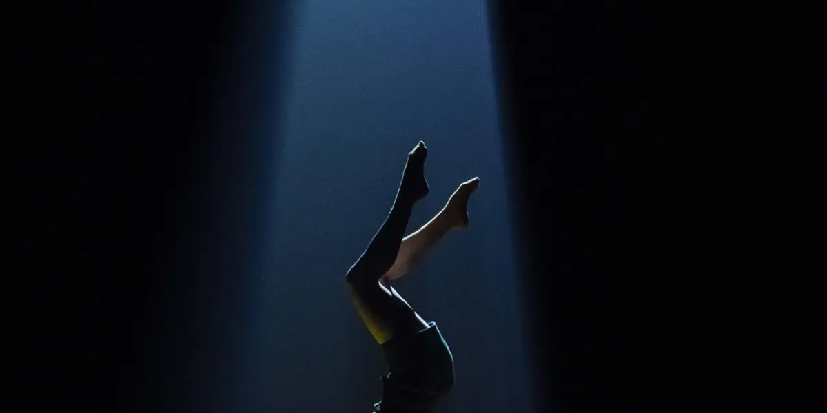 Emma Verhaeghe se tient en équilibre sur la tête au sommet d'une plate-forme jaune, éclairée par un projecteur dramatique sur un fond sombre.