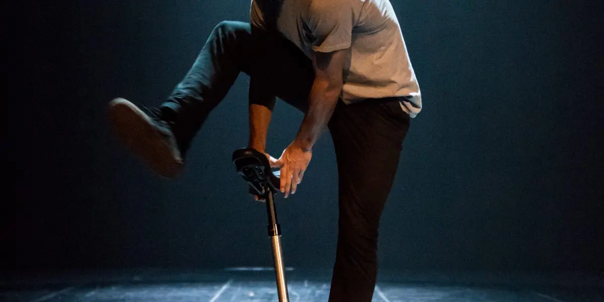 Ruben Ingwersen exécute un tour sur un monocycle sous un éclairage dramatique, en équilibre avec une jambe tendue tout en traversant une scène sombre et éclairée par des projecteurs.