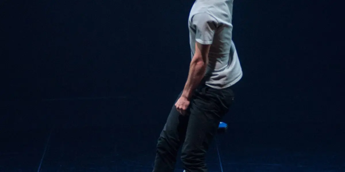 Ruben Ingwersen se tient en équilibre sur un monocycle sur une scène sombre, penché d'un côté, un bras levé et l'autre baissé, semblant exécuter un tour sous un éclairage dramatique.