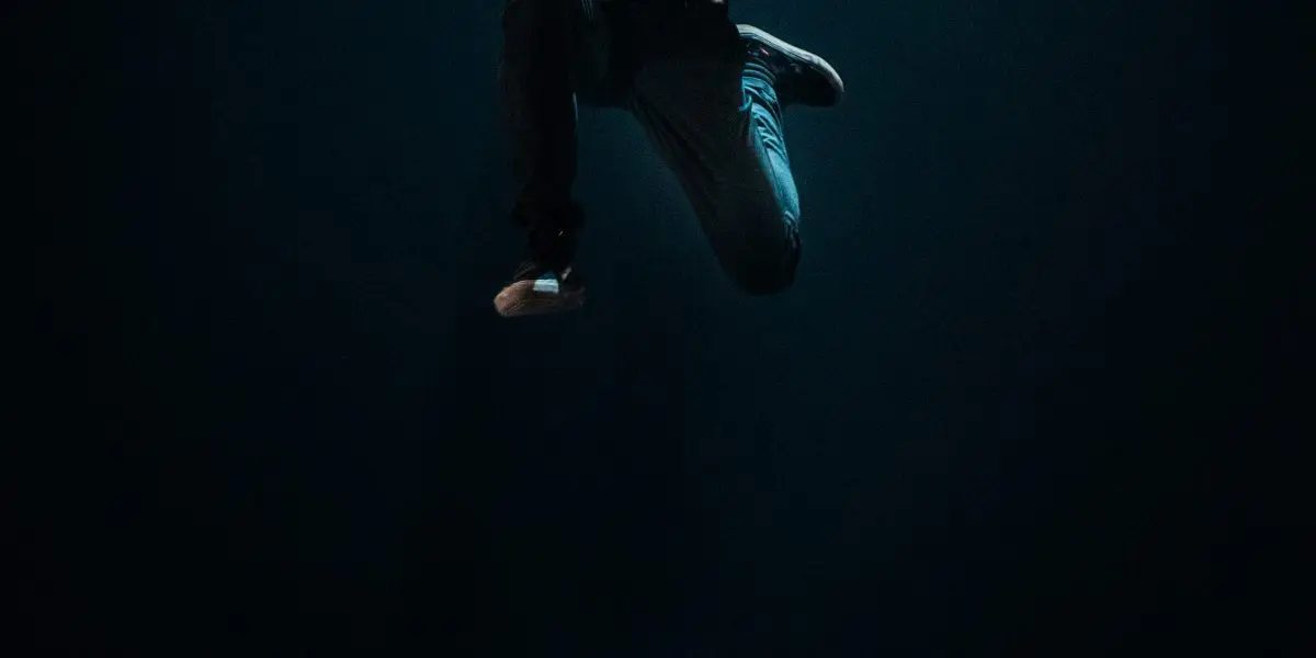 Une personne saute spectaculairement en l'air au-dessus d'un petit vélo, éclairé par un projecteur sur une scène sombre. Rappelant le style caractéristique de Ruben Ingwersen, le vélo semble être en mouvement et projette une ombre sur le sol.