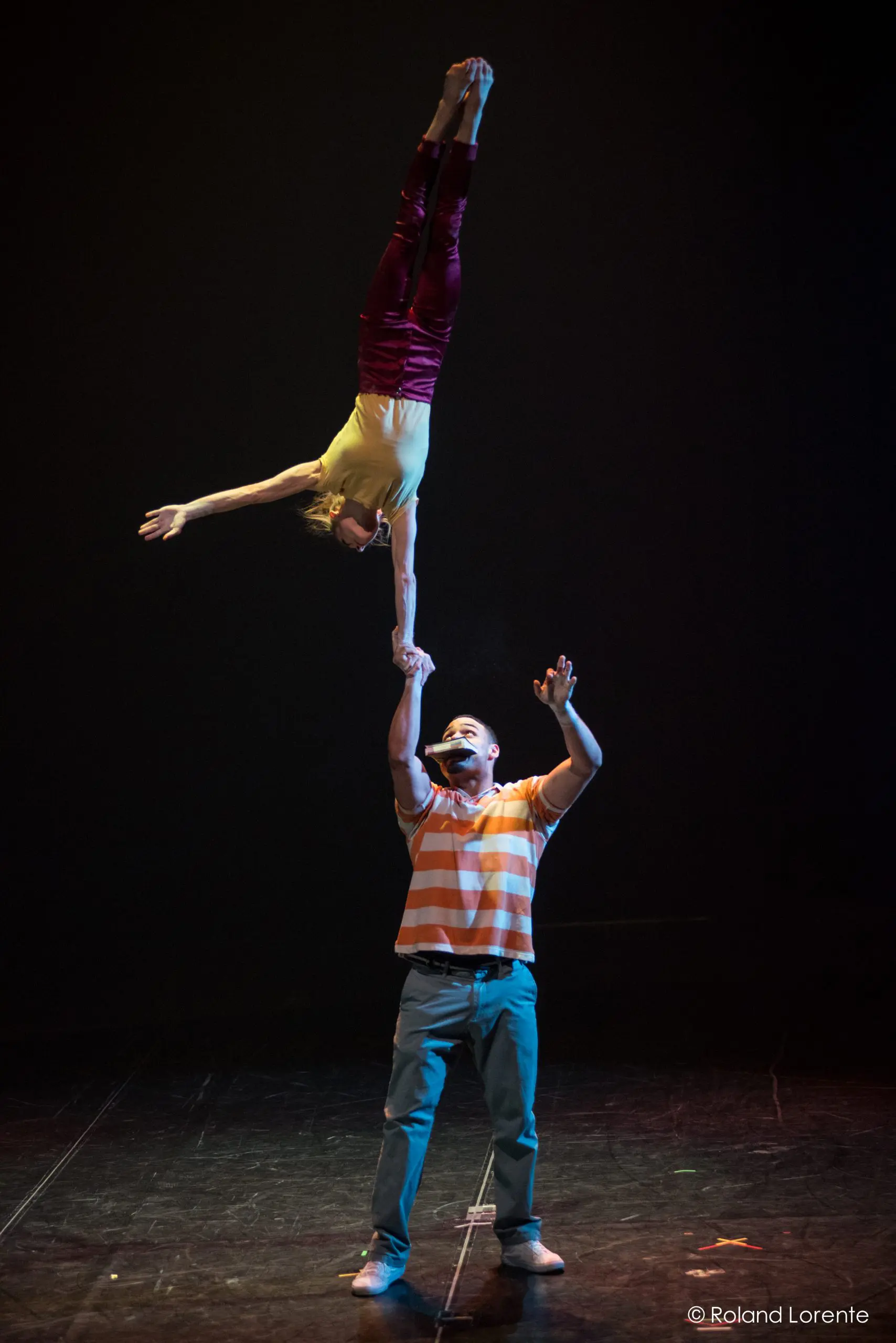 Joëlle Ziorjen et Michael Patterson sont captivants : il la fait tenir en équilibre sur une main, son corps étendu à la verticale au-dessus de lui, tandis qu'ils se produisent sur une scène sombre sous un éclairage dramatique.