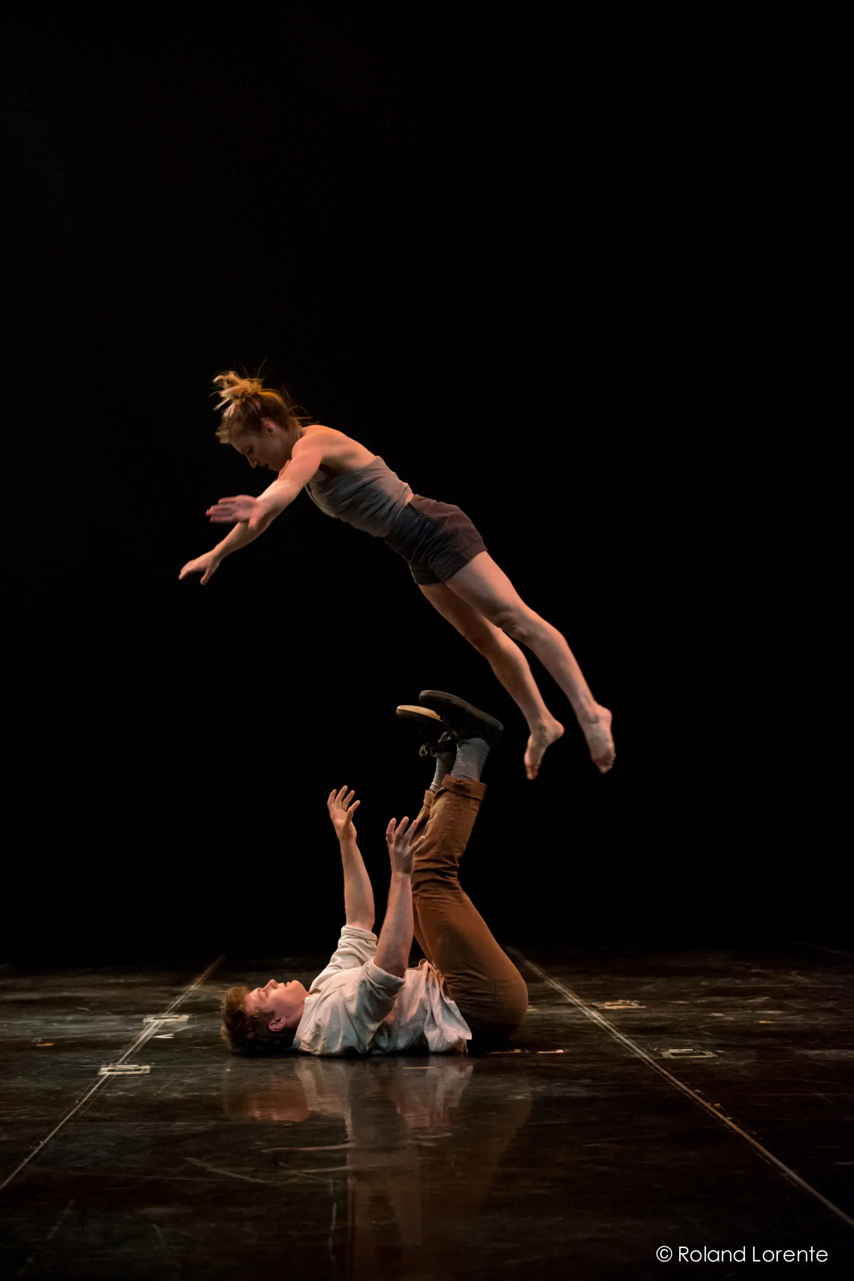 Andrei Anissimov et Emma Rogers se produisent alors qu'une danseuse s'envole, bras tendus, au-dessus d'un danseur allongé sur le dos, la soulevant avec ses pieds et ses mains lors d'un spectacle de danse contemporaine sur une scène faiblement éclairée.