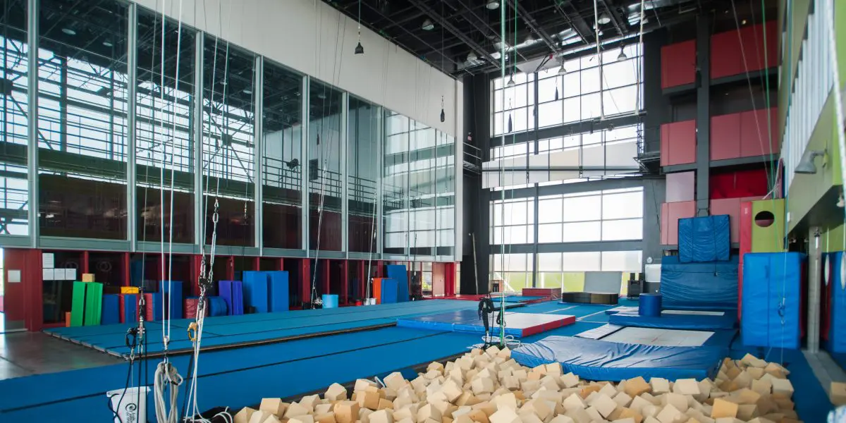 Un spacieux centre d'entraînement à la gymnastique en salle offre des services aux artistes de cirque professionnel. Il comprend une fosse à mousse, des tapis bleus, des cordes à grimper, des poutres d'équilibre et de grandes fenêtres. Les murs sont recouverts d'un rembourrage coloré pour plus de sécurité.
