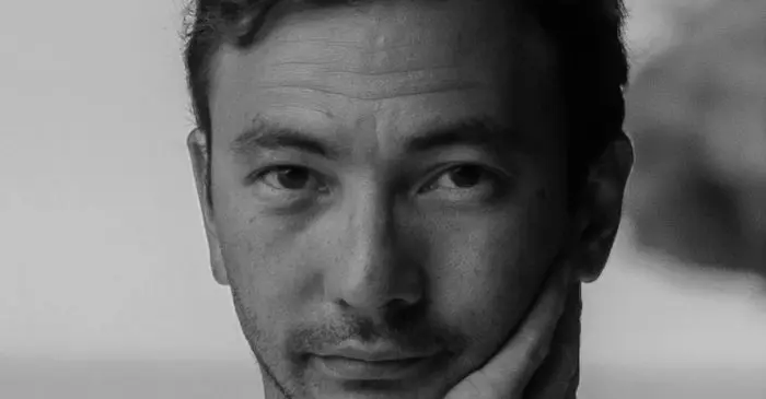 Portrait en noir et blanc de Jame Tanabe, directeur des études à l'ECN. Cheveux courts et chemise claire, il appuie son visage sur sa main droite et regarde l'appareil photo d'un air pensif.