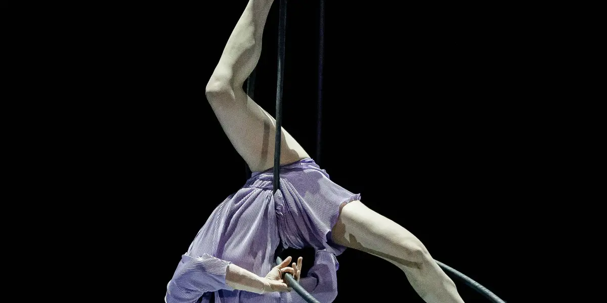 L'artiste aérienne Katarina Sobinkovicova, vêtue d'un costume violet, est suspendue à l'envers à un cerceau, qu'elle agrippe d'une jambe et d'un bras, sur un fond noir.