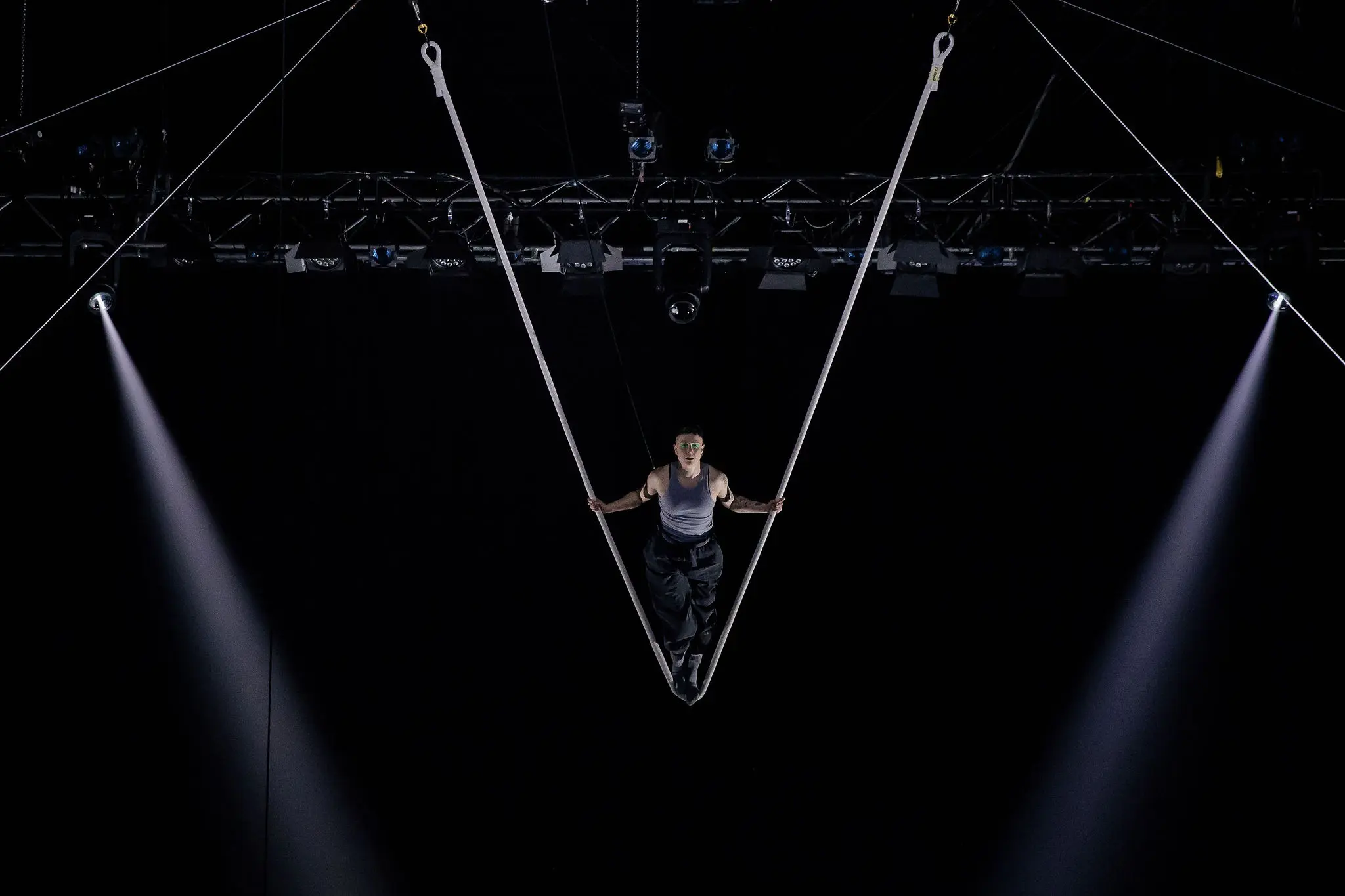 Nin Khelifa se produit sur des sangles aériennes, suspendues en forme de V au-dessus d'une scène sombre, avec des projecteurs qui brillent de part et d'autre.