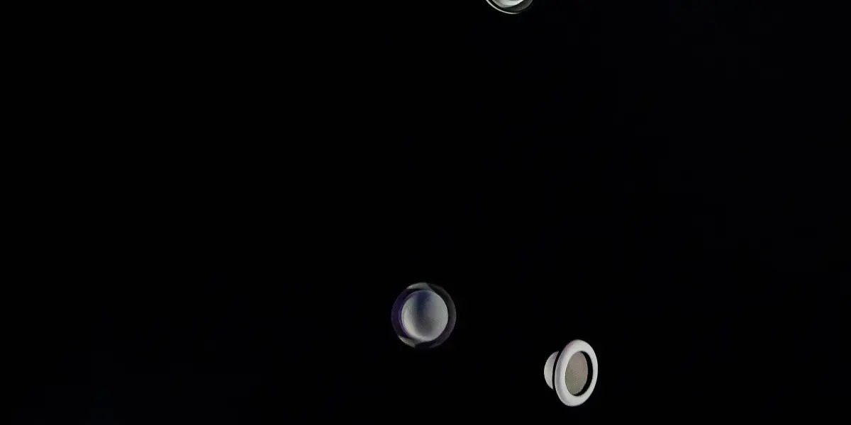 William Borges, un artiste sur une scène faiblement éclairée, jongle habilement avec quatre chapeaux blancs dans les airs, avec une chaise vide en arrière-plan et un éclairage dramatique soulignant l'action.