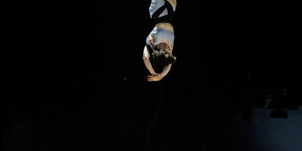 Une artiste vêtue d'un costume blanc est suspendue à l'envers, enveloppée de soies aériennes, dans les airs sur un fond sombre - un spectacle époustouflant de Sara Sabina Arizmendi Fernandez.