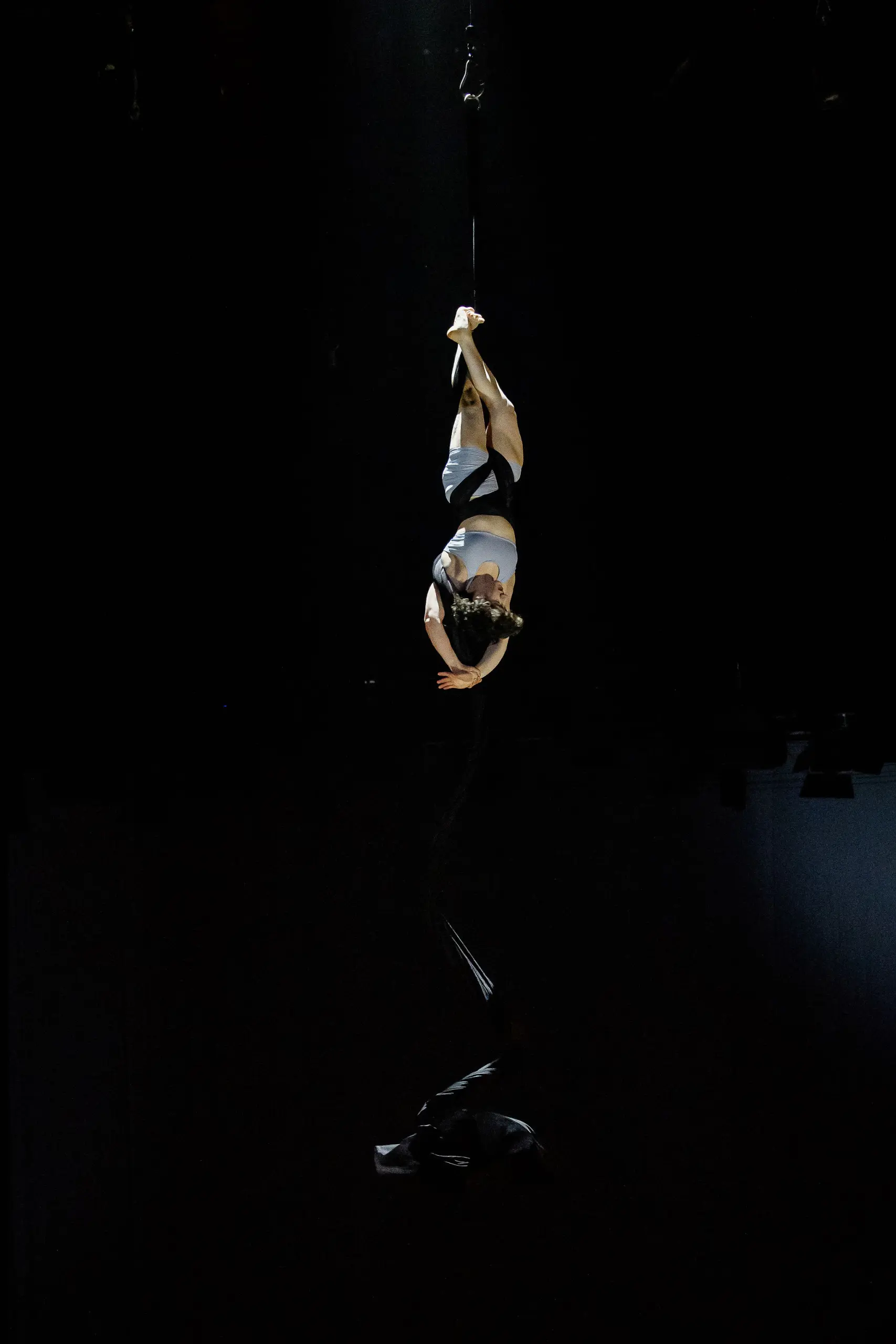Une artiste vêtue d'un costume blanc est suspendue à l'envers, enveloppée de soies aériennes, dans les airs sur un fond sombre - un spectacle époustouflant de Sara Sabina Arizmendi Fernandez.