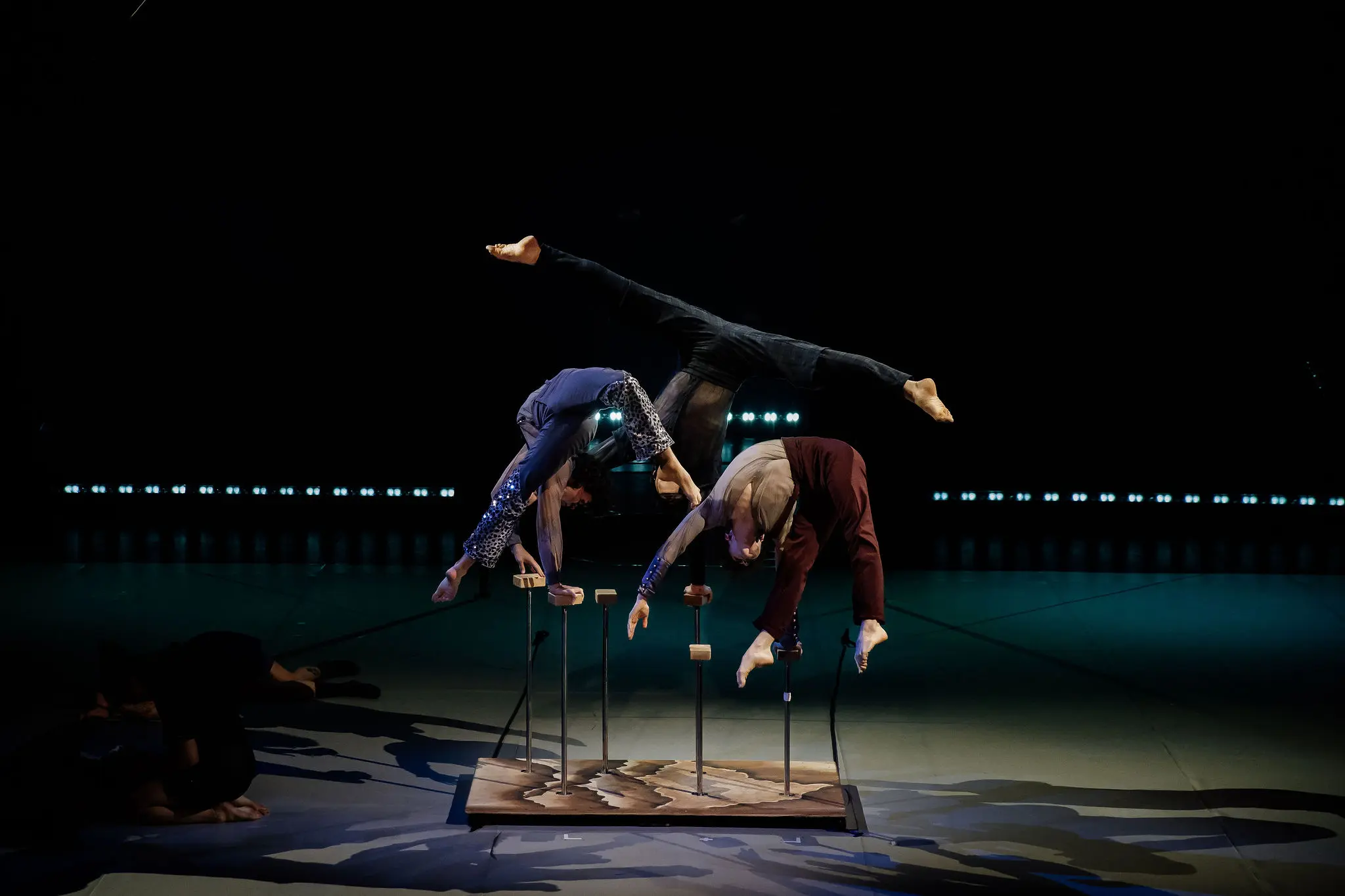 Deux acrobates se tiennent en équilibre sur des cannes, le corps arqué dans des directions opposées et les jambes tendues en l'air, sous un éclairage dramatique pendant les matinées animées.