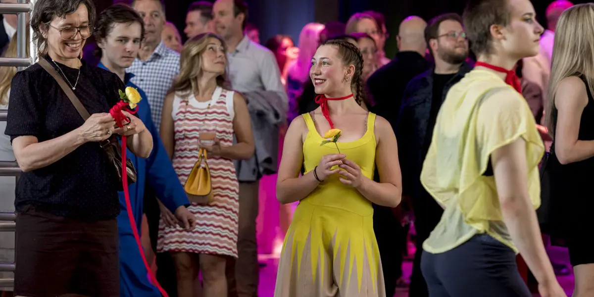 Un groupe de personnes lors d'une soirée-bénéfice en salle de la Fondation de l'ENC ; certains sont habillés de façon décontractée tandis que d'autres portent des costumes jaune vif et tiennent des fleurs jaunes, avec un éclairage coloré en arrière-plan.