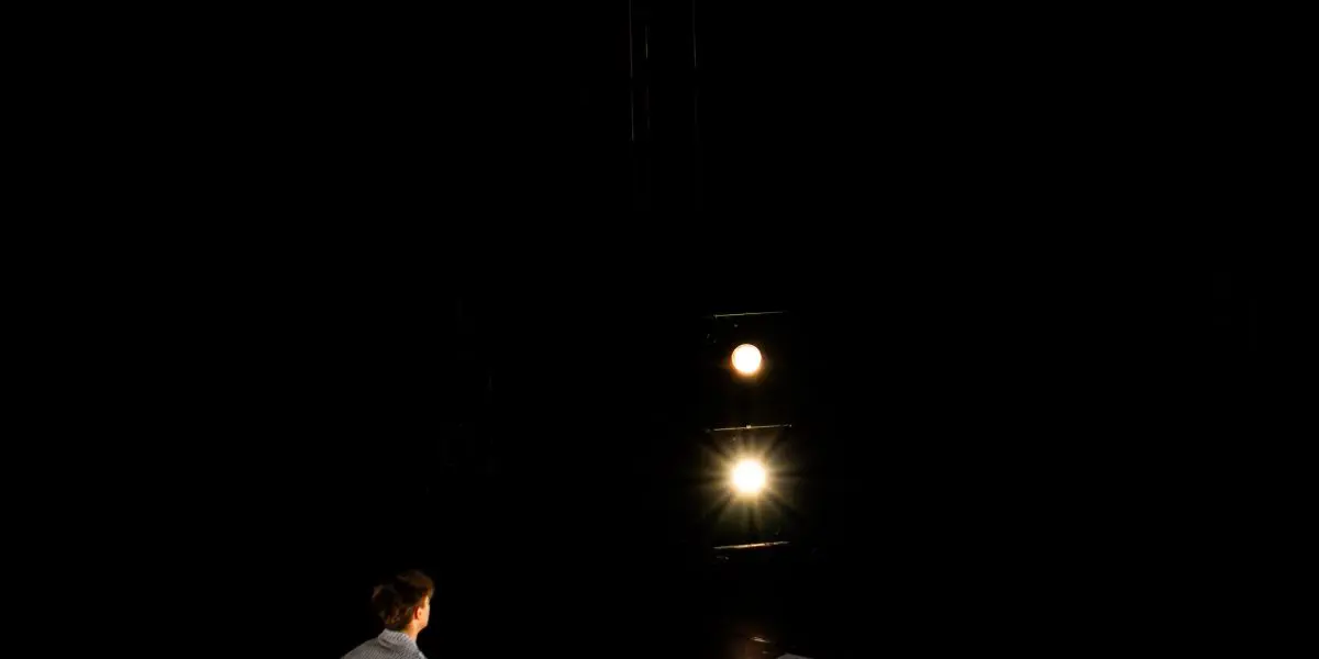 Un athlète de TriSwiss exécute un saut périlleux arrière en l'air au-dessus d'un appareil ressemblant à une balançoire, tandis qu'une autre personne se tient en dessous, regardant vers le haut, le tout sur un fond sombre avec un éclairage dramatique.