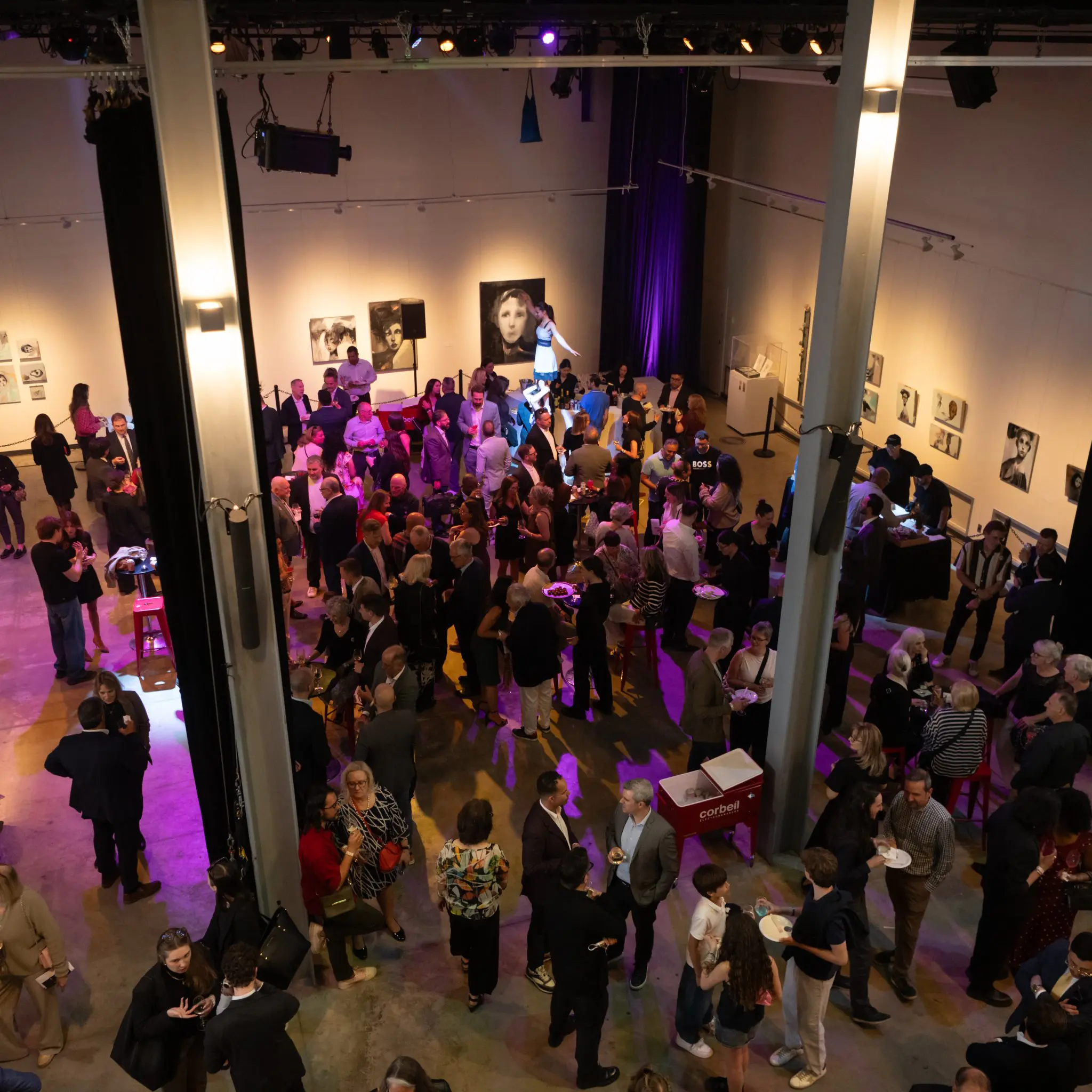 Une foule nombreuse se rassemble lors d'un événement organisé dans une galerie d'art, où les invités discutent et admirent des portraits sous un éclairage intense. L'effervescence règne dans cette salle spacieuse alors que se répand la nouvelle de deux subventions majeures accordées au Centre de recherche sur le potentiel humain.