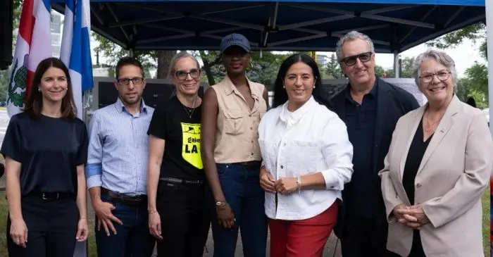 Sept personnes se tiennent côte à côte, souriantes, devant un auvent bleu en plein air ; elles portent des tenues décontractées ou semi-formelles, avec des drapeaux et des arbres visibles en arrière-plan, et célèbrent le succès de « La Soirée-bénéfice 2026 », qui a permis de récolter 150 000 dollars pour soutenir la prochaine génération à l’École nationale de cirque.