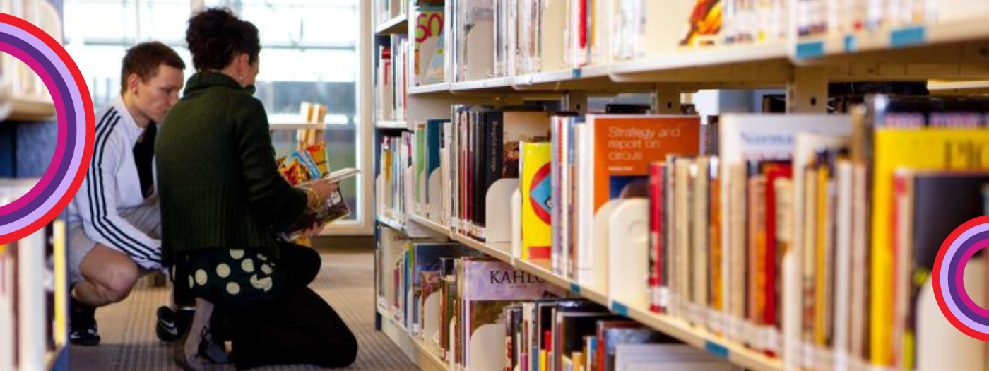 Deux personnes sont agenouillées entre les étagères d'une bibliothèque et regardent ensemble des livres. Des livres aux couleurs vives sont soigneusement rangés, avec des dessins circulaires dans les coins, célébrant la Journée canadienne des employés des bibliothèques.