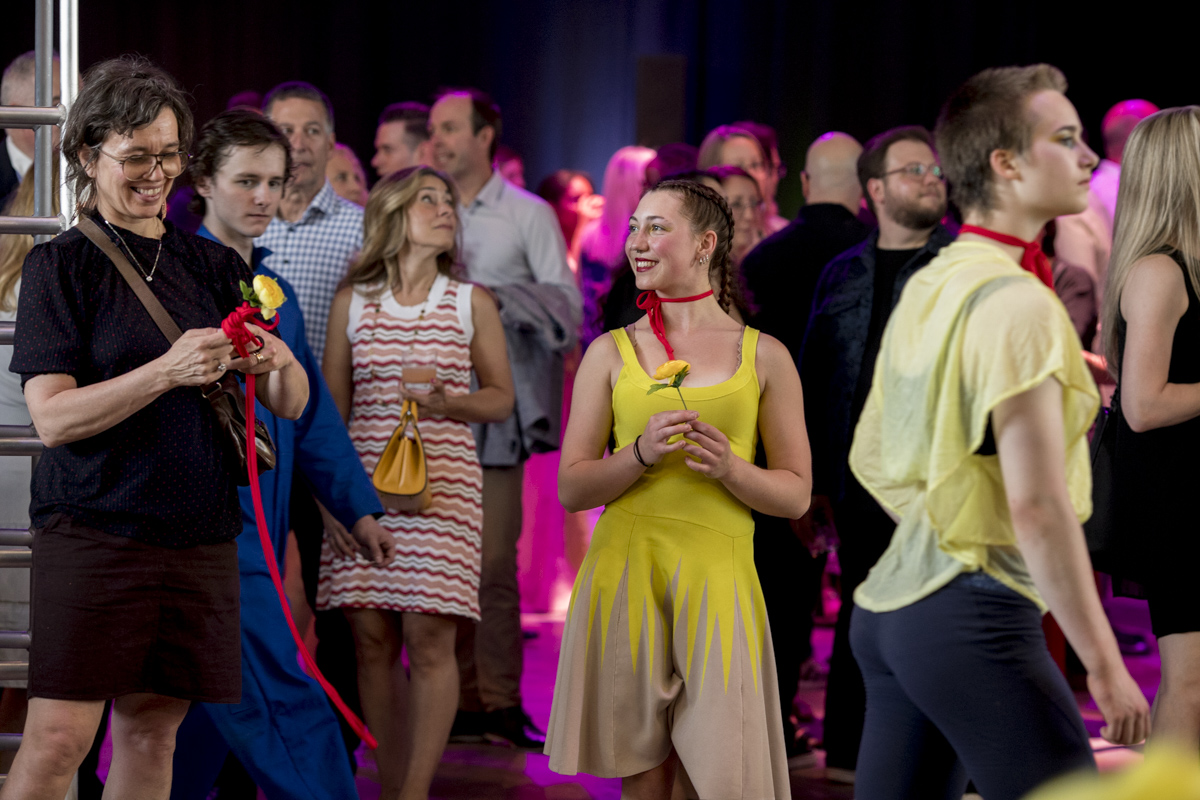 Un groupe de personnes lors d'une soirée-bénéfice en salle de la Fondation de l'ENC ; certains sont habillés de façon décontractée tandis que d'autres portent des costumes jaune vif et tiennent des fleurs jaunes, avec un éclairage coloré en arrière-plan.