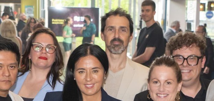 Un groupe de douze personnes, élégamment vêtues en tenue professionnelle ou semi-formelle, sourient pour une photo lors de la Soirée-bénéfice 2026, au cours de laquelle 150 000 dollars ont été récoltés pour soutenir la prochaine génération à l’École nationale de cirque. Des affiches et une enseigne de bistrot ajoutent du charme à cet espace événementiel moderne.